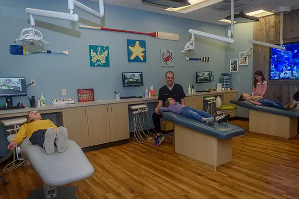 A smiling Dr. Eric Jacobsen at the dental office with young happy patients each sitting in their own dentist chair