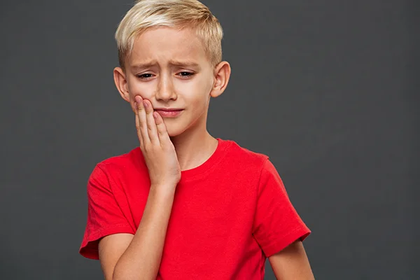 Child wearing red shirt touching jaw to indicate aching