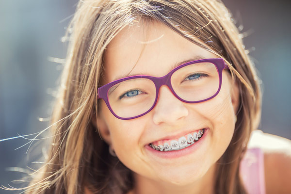 Young blonde girl with glasses smiling with her braces