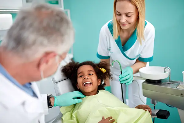 Adorable and young girl sitting in a dental chair and smiling at her dentist and dental assistant