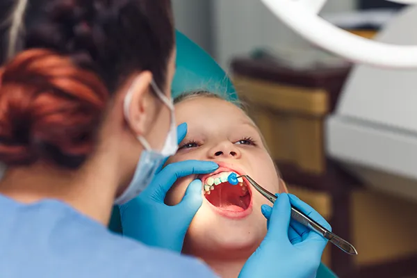 Young boy patiently keeping his mouth open while his dentist applies fluoride solution to his teeth