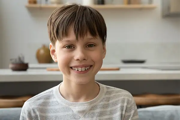 Happy young boy showing his braces while sitting at home, emphasizing the importance of early orthodontic intervention.